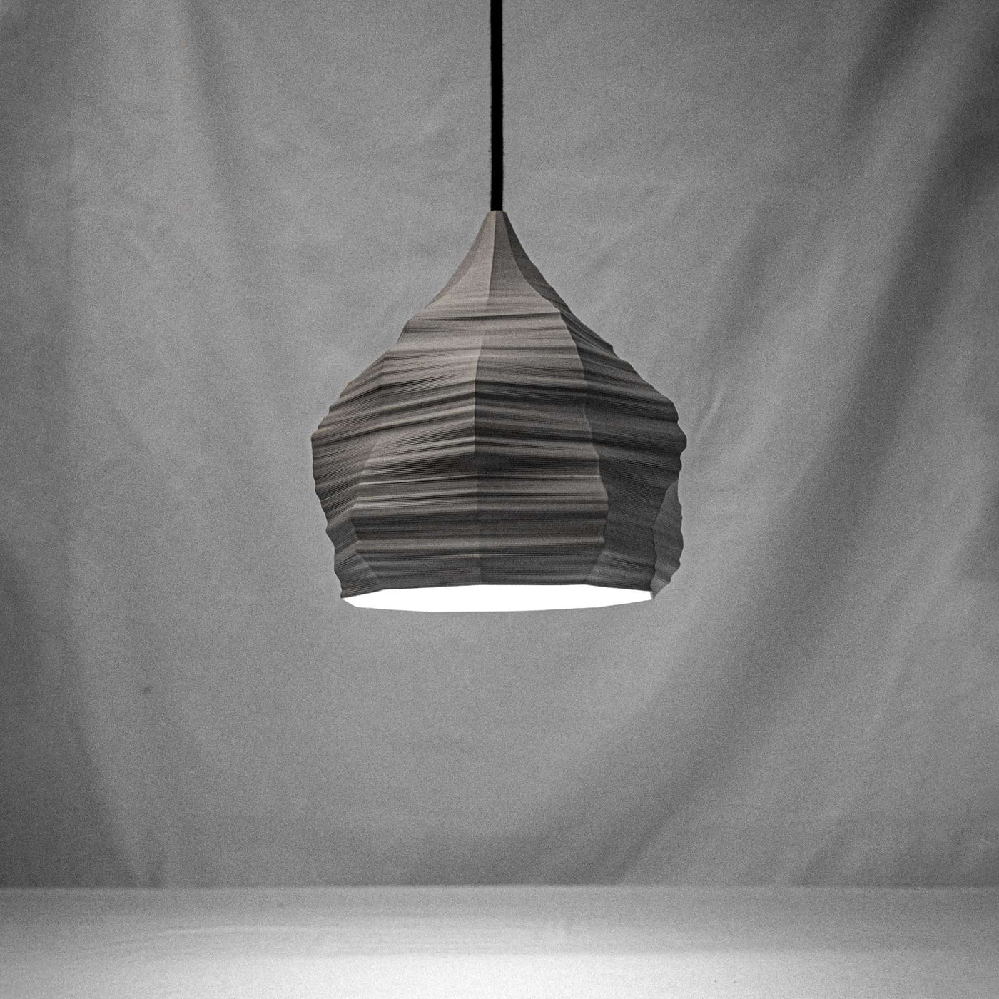 A 3D printed ambient lamp, pleated pendant lampshade with a LED light at the bottom, suspended by a cable against a neutral background.