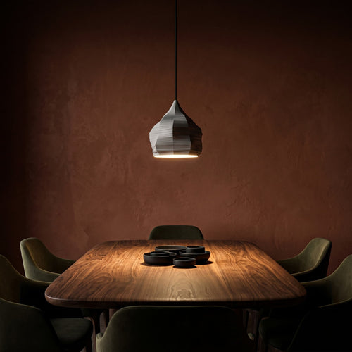 Dunalia pendant lamp against a dark red brown wall. Dining area with a wooden table and chairs.