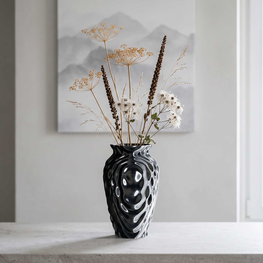 ONDA Resonance 3D-printed vase in black and silver with dried wild flowers on a stone shelf in a bright interior